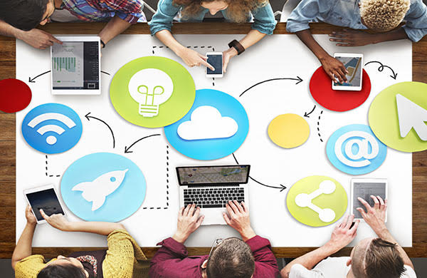 Birds eye view of six people sitting at a table, each with digital devices. The image sets the theme of digital futures.