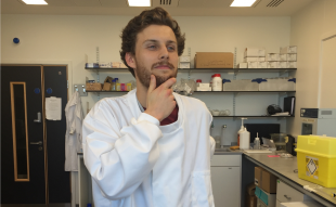PhD placement student Michael Norman posing for the camera in the laboratory in his white lab coat.
